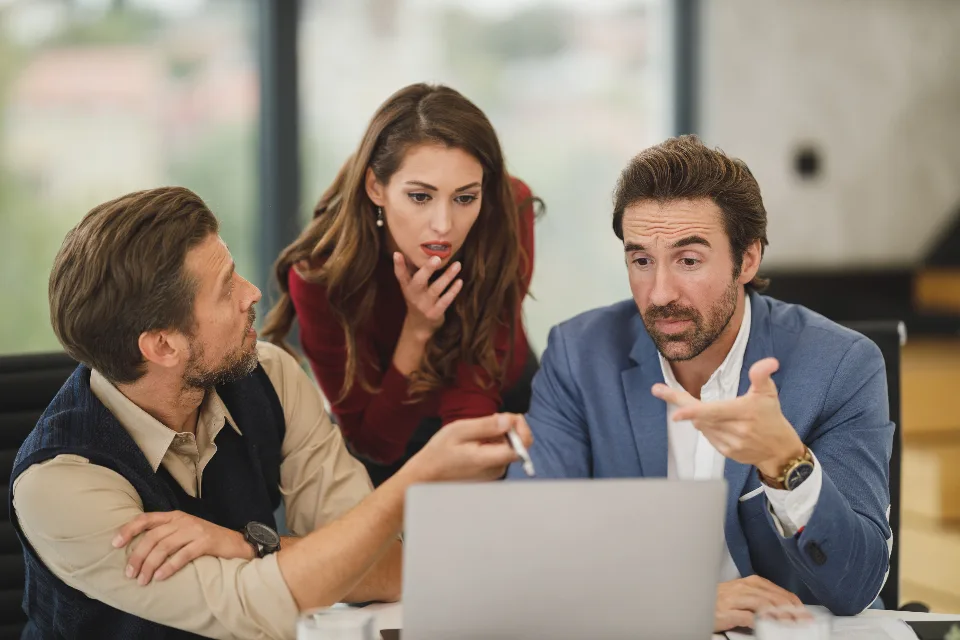 Equipe de profissionais reunida analisando um notebook em uma sala de reuniões.