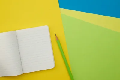 Caderno aberto e lápis sobre um fundo colorido.
